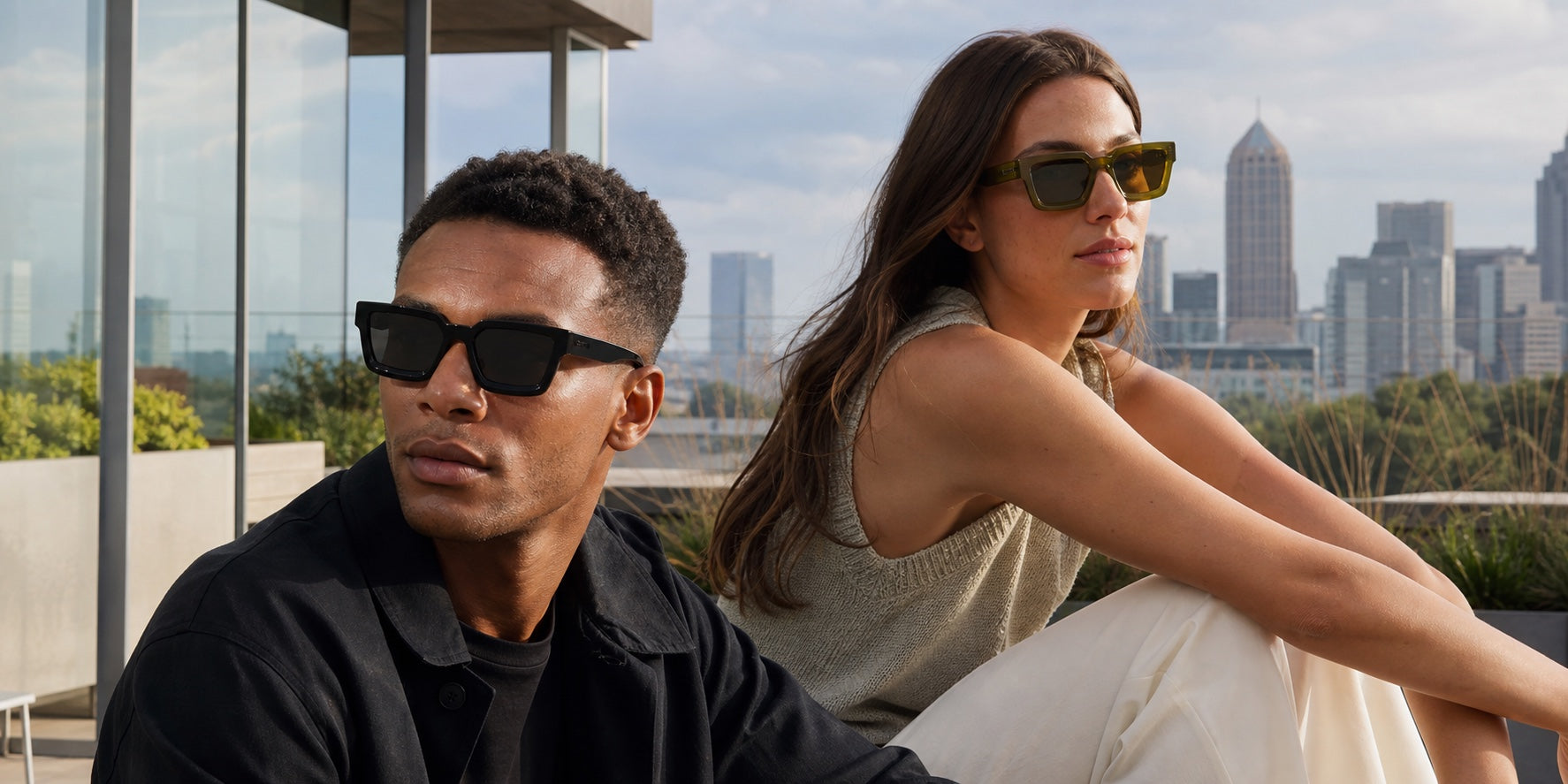 A man and woman wearing The Herald sunglasses on a refined rooftop terrace